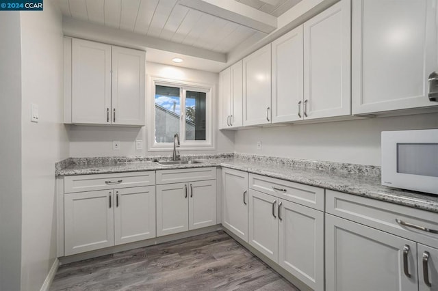 kitchen featuring white cabinetry, sink, light stone counters, and hardwood / wood-style flooring