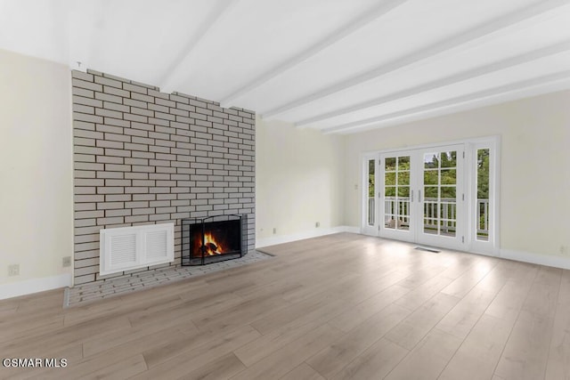 unfurnished living room featuring beamed ceiling, light wood-type flooring, a fireplace, and french doors