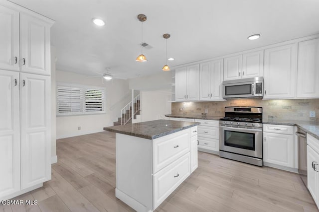 kitchen featuring appliances with stainless steel finishes, white cabinetry, a kitchen island, decorative light fixtures, and dark stone counters