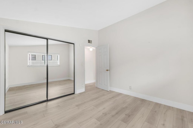 unfurnished bedroom with vaulted ceiling, a closet, and light wood-type flooring