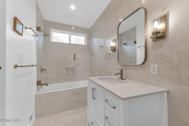 bathroom with tile walls, vanity, and tiled shower / bath combo