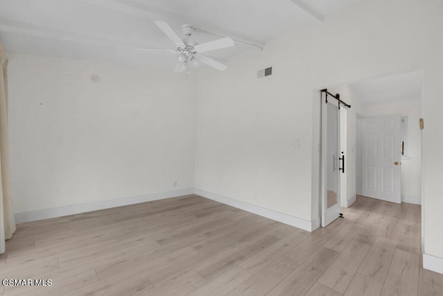 empty room featuring ceiling fan, a barn door, beam ceiling, and light hardwood / wood-style floors