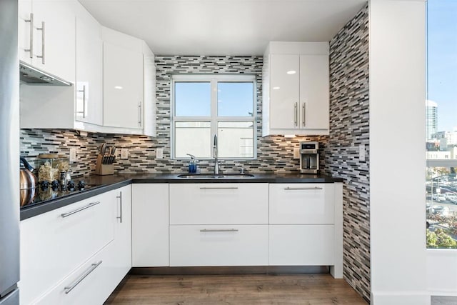 kitchen with black electric stovetop, backsplash, dark hardwood / wood-style flooring, white cabinets, and sink