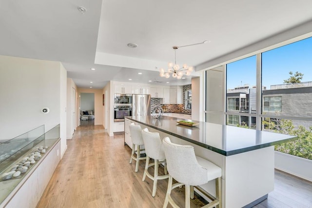 kitchen featuring pendant lighting, white cabinetry, an inviting chandelier, tasteful backsplash, and stainless steel fridge