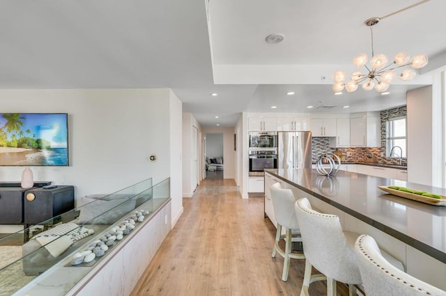 kitchen featuring an inviting chandelier, decorative backsplash, decorative light fixtures, stainless steel refrigerator, and white cabinets