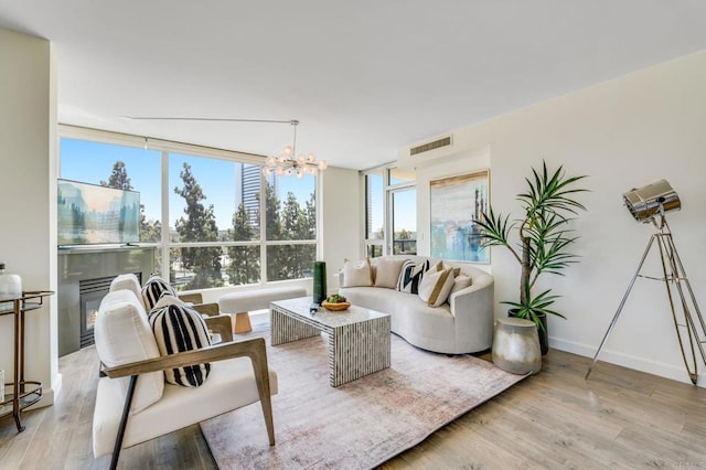 living room with a wall of windows, a healthy amount of sunlight, a notable chandelier, and light hardwood / wood-style flooring