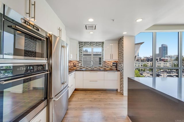 kitchen with white cabinetry, stainless steel appliances, decorative backsplash, light hardwood / wood-style flooring, and sink