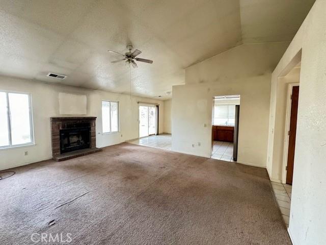 unfurnished living room with a fireplace, ceiling fan, lofted ceiling, and light carpet