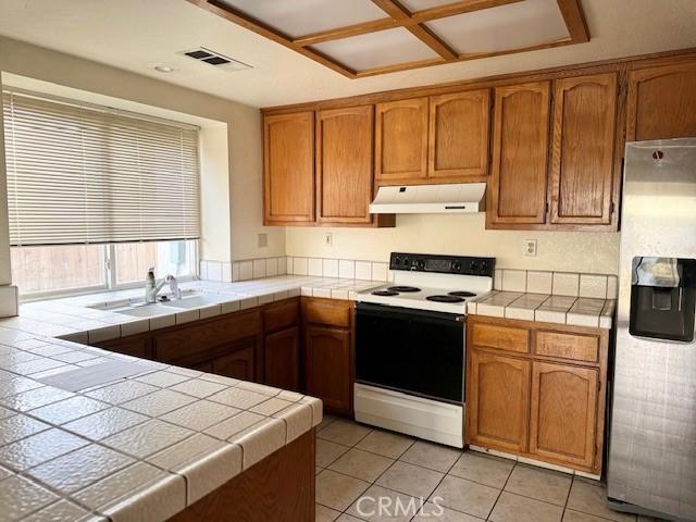 kitchen with white electric range oven, stainless steel refrigerator with ice dispenser, tile counters, and sink