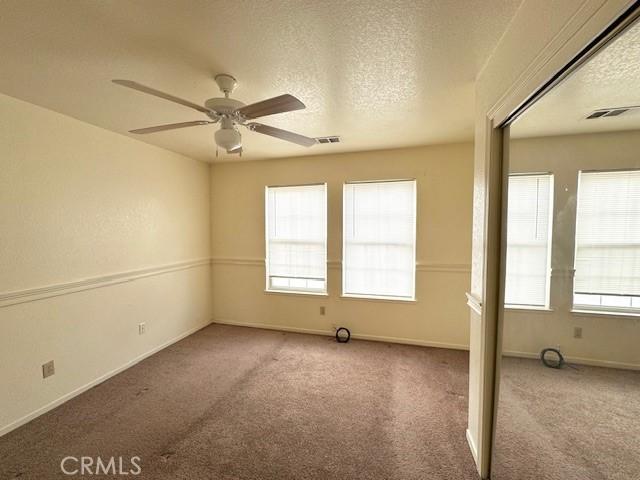 carpeted spare room with ceiling fan, a healthy amount of sunlight, and a textured ceiling