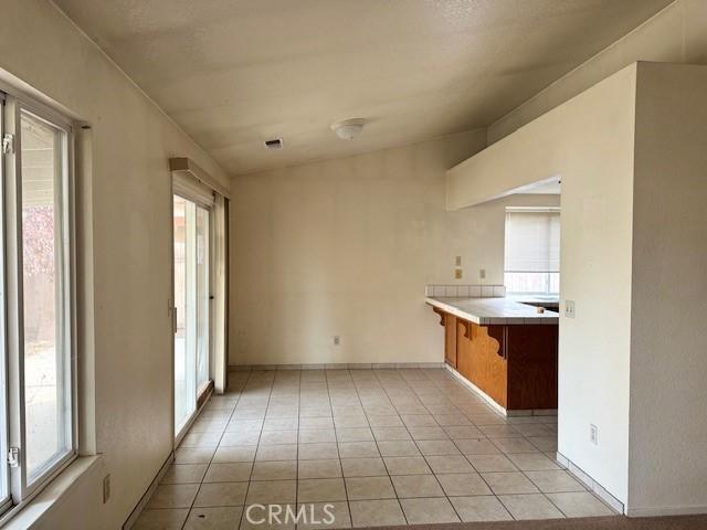 kitchen featuring tile counters, light tile patterned floors, kitchen peninsula, and vaulted ceiling