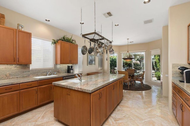 kitchen with light stone countertops, sink, tasteful backsplash, pendant lighting, and a center island with sink