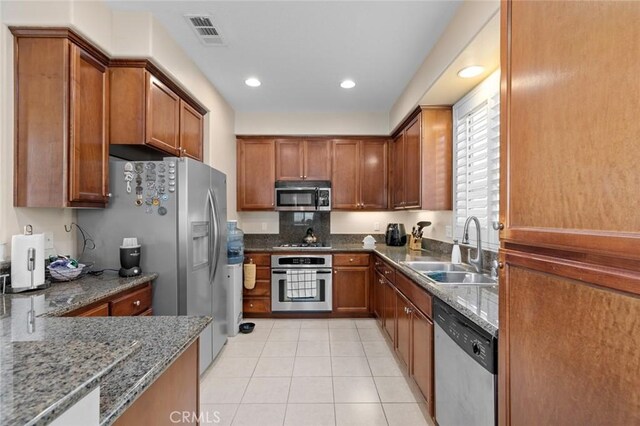 kitchen featuring dark stone countertops, sink, light tile patterned floors, and appliances with stainless steel finishes