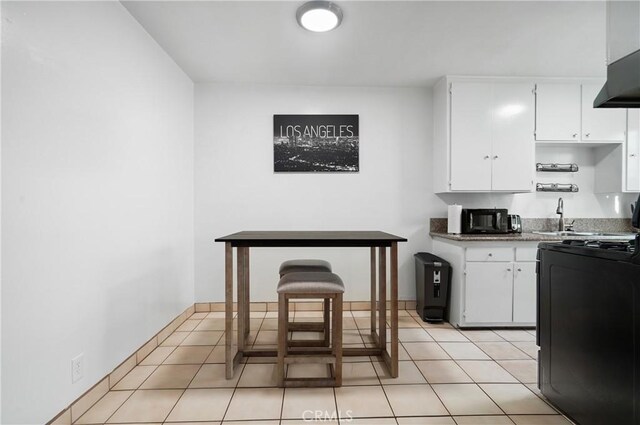 kitchen with white cabinets, range, sink, light tile patterned floors, and range hood