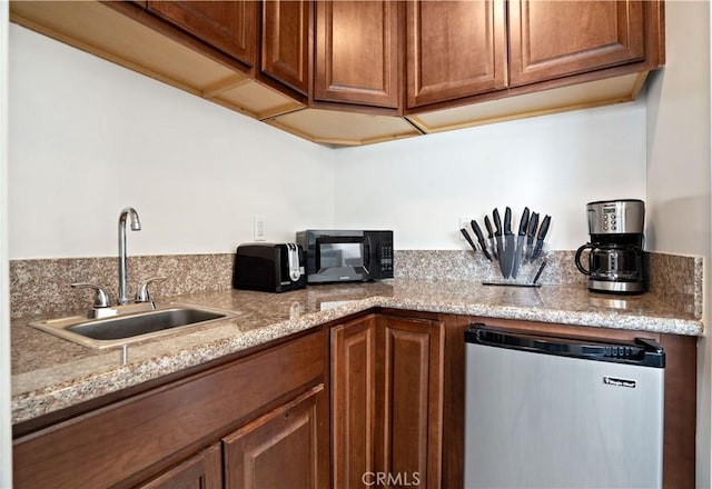 kitchen featuring sink, refrigerator, and light stone counters