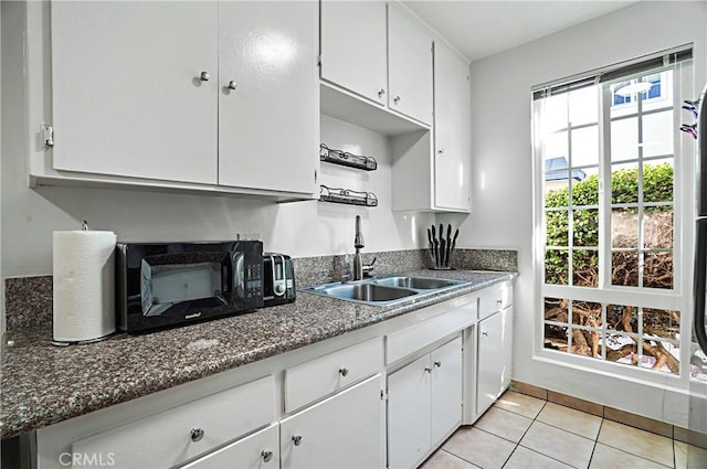 kitchen featuring sink, white cabinetry, light tile patterned floors, and dark stone countertops