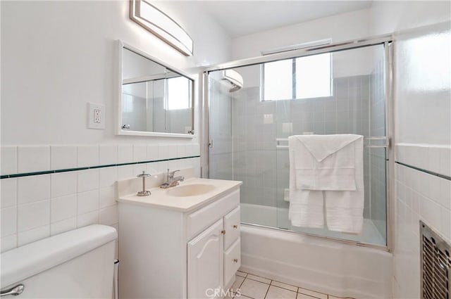 full bathroom featuring shower / bath combination with glass door, tile patterned flooring, vanity, tile walls, and toilet