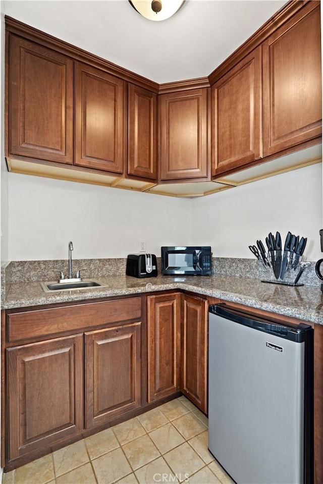 kitchen with light tile patterned floors, sink, stainless steel fridge, and light stone countertops