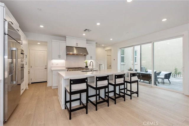 kitchen featuring a breakfast bar, a kitchen island with sink, light wood-type flooring, white cabinetry, and stainless steel appliances