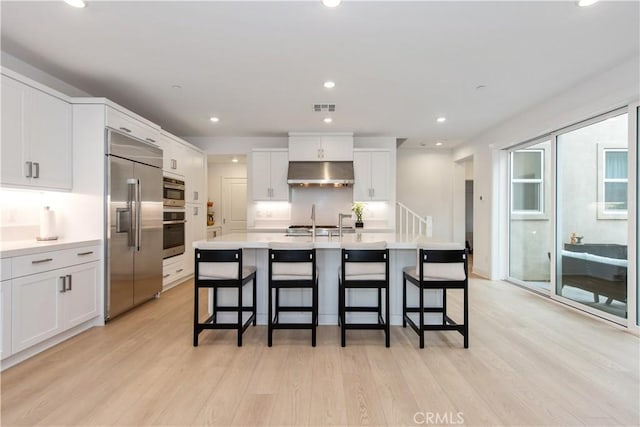 kitchen featuring white cabinets, an island with sink, appliances with stainless steel finishes, light hardwood / wood-style floors, and a kitchen bar