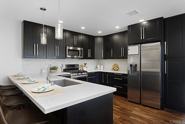 kitchen featuring appliances with stainless steel finishes, a kitchen bar, sink, hanging light fixtures, and kitchen peninsula