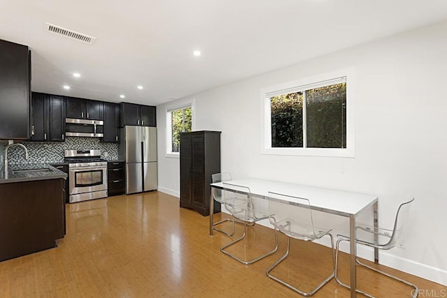 kitchen with appliances with stainless steel finishes, light hardwood / wood-style floors, tasteful backsplash, and sink