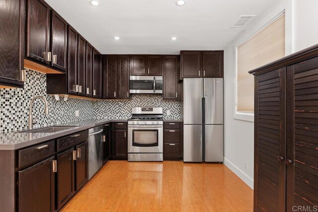 kitchen featuring backsplash, sink, dark brown cabinetry, light wood-type flooring, and stainless steel appliances