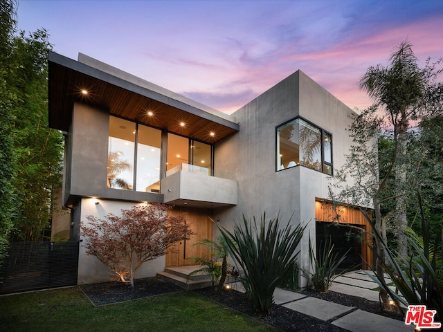 back house at dusk with a balcony and a garage