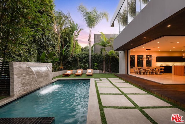 pool at dusk featuring pool water feature, a patio, and a wooden deck