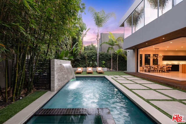 pool at dusk featuring a patio area, an in ground hot tub, and pool water feature