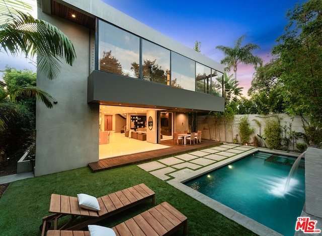 back house at dusk featuring a lawn, a fenced in pool, and a patio