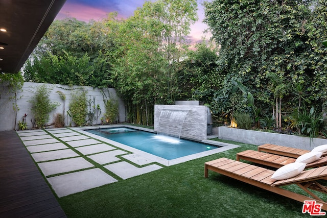 pool at dusk featuring a jacuzzi and pool water feature