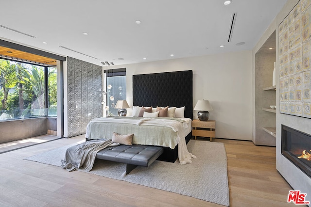 bedroom with a wall of windows, light wood-type flooring, and a fireplace