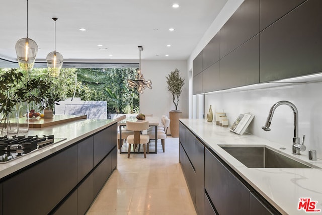 kitchen with light stone counters, sink, decorative light fixtures, and gas stovetop