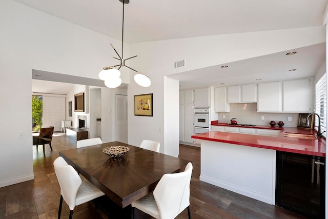 dining area with a chandelier, sink, wine cooler, and dark wood-type flooring