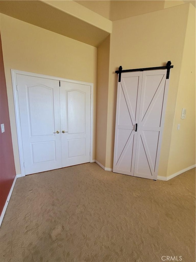 unfurnished bedroom featuring light carpet, a barn door, and a closet