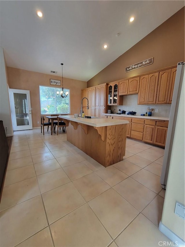 kitchen featuring a center island with sink, hanging light fixtures, vaulted ceiling, light tile patterned floors, and a notable chandelier