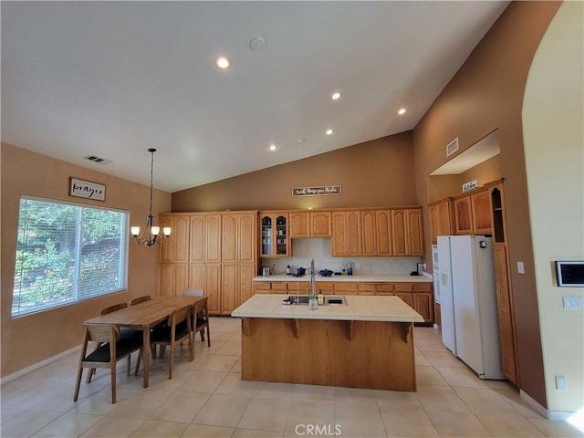 kitchen with sink, white refrigerator with ice dispenser, a chandelier, vaulted ceiling, and a center island with sink