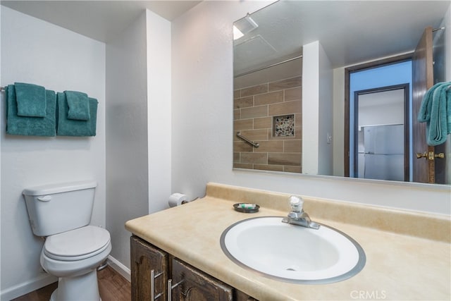 bathroom featuring tiled shower, wood-type flooring, vanity, and toilet