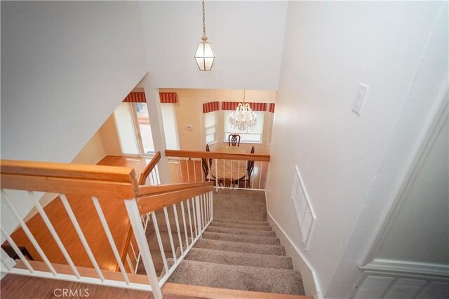 staircase with hardwood / wood-style flooring, a high ceiling, and an inviting chandelier