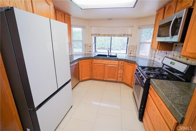 kitchen with dark stone counters, sink, appliances with stainless steel finishes, tasteful backsplash, and light tile patterned flooring