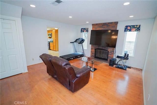 living room with a fireplace, a textured ceiling, and light hardwood / wood-style flooring