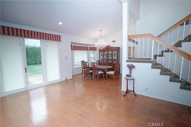 dining area featuring hardwood / wood-style floors, vaulted ceiling, and an inviting chandelier