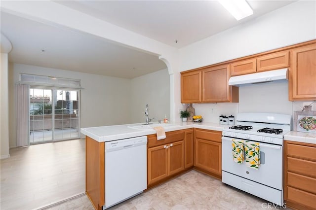 kitchen with kitchen peninsula, white appliances, tile counters, and sink