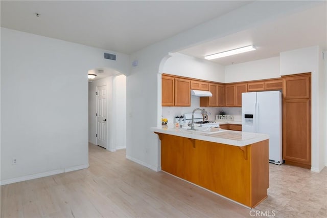 kitchen with kitchen peninsula, white appliances, decorative backsplash, a breakfast bar, and light wood-type flooring