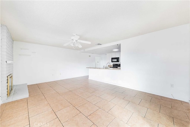 unfurnished living room featuring a textured ceiling, a fireplace, sink, ceiling fan, and light tile patterned floors