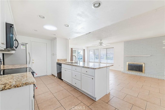 kitchen featuring a brick fireplace, kitchen peninsula, sink, black dishwasher, and white cabinetry