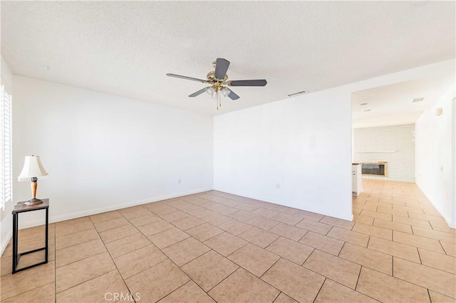 unfurnished room featuring a textured ceiling, ceiling fan, light tile patterned floors, and a fireplace