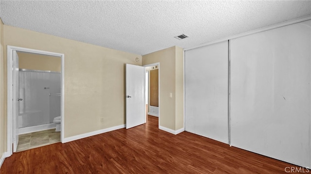 unfurnished bedroom featuring a textured ceiling, a closet, connected bathroom, and hardwood / wood-style flooring