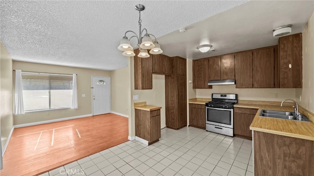 kitchen featuring a notable chandelier, pendant lighting, stainless steel gas range oven, sink, and light tile patterned floors